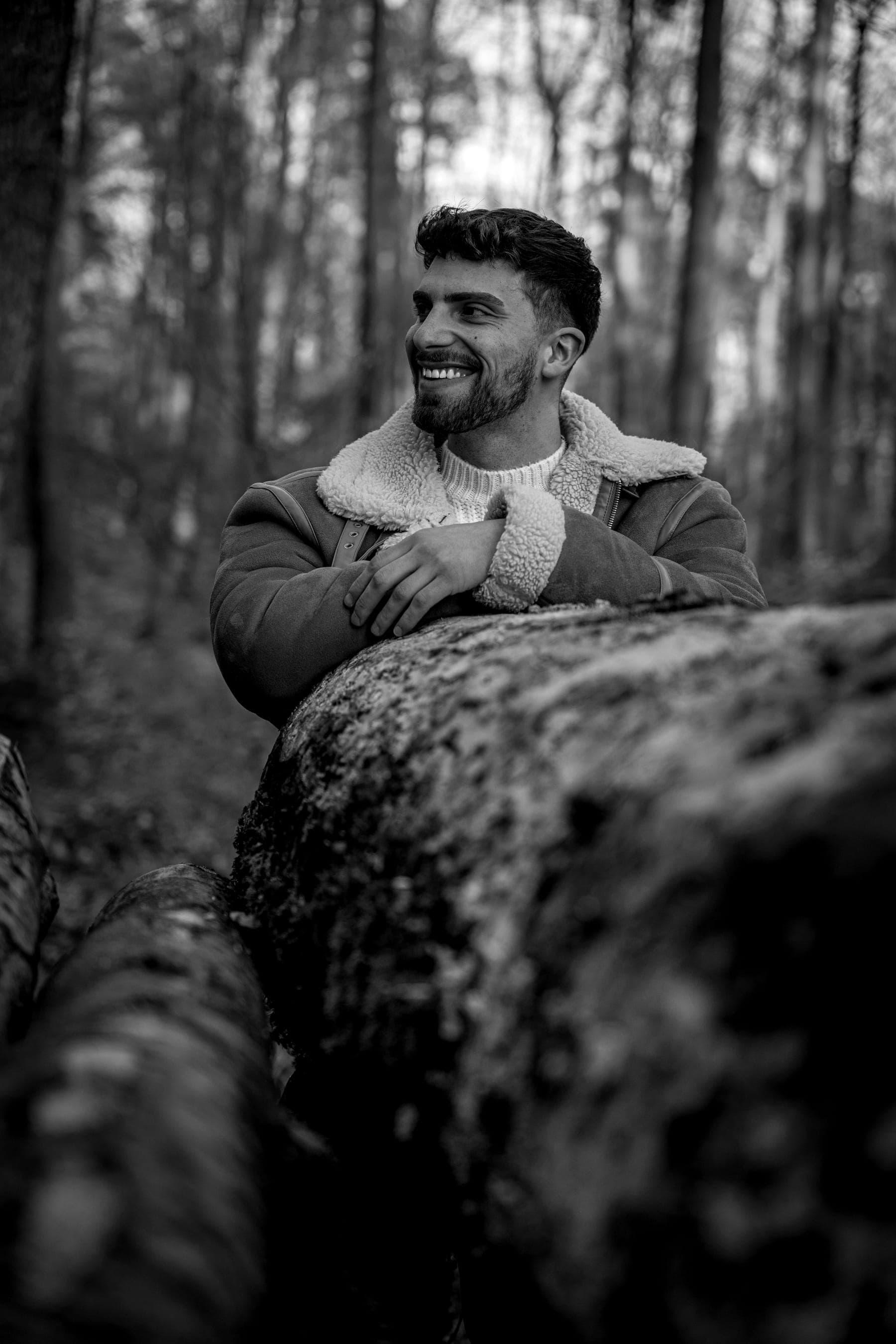 Luis Grau lachend im Wald, auf einen Baumstamm gestützt